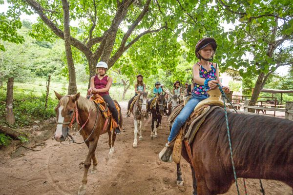 Niño montando a caballo con casco en el tour en caballo familiar de Rancho Capomo